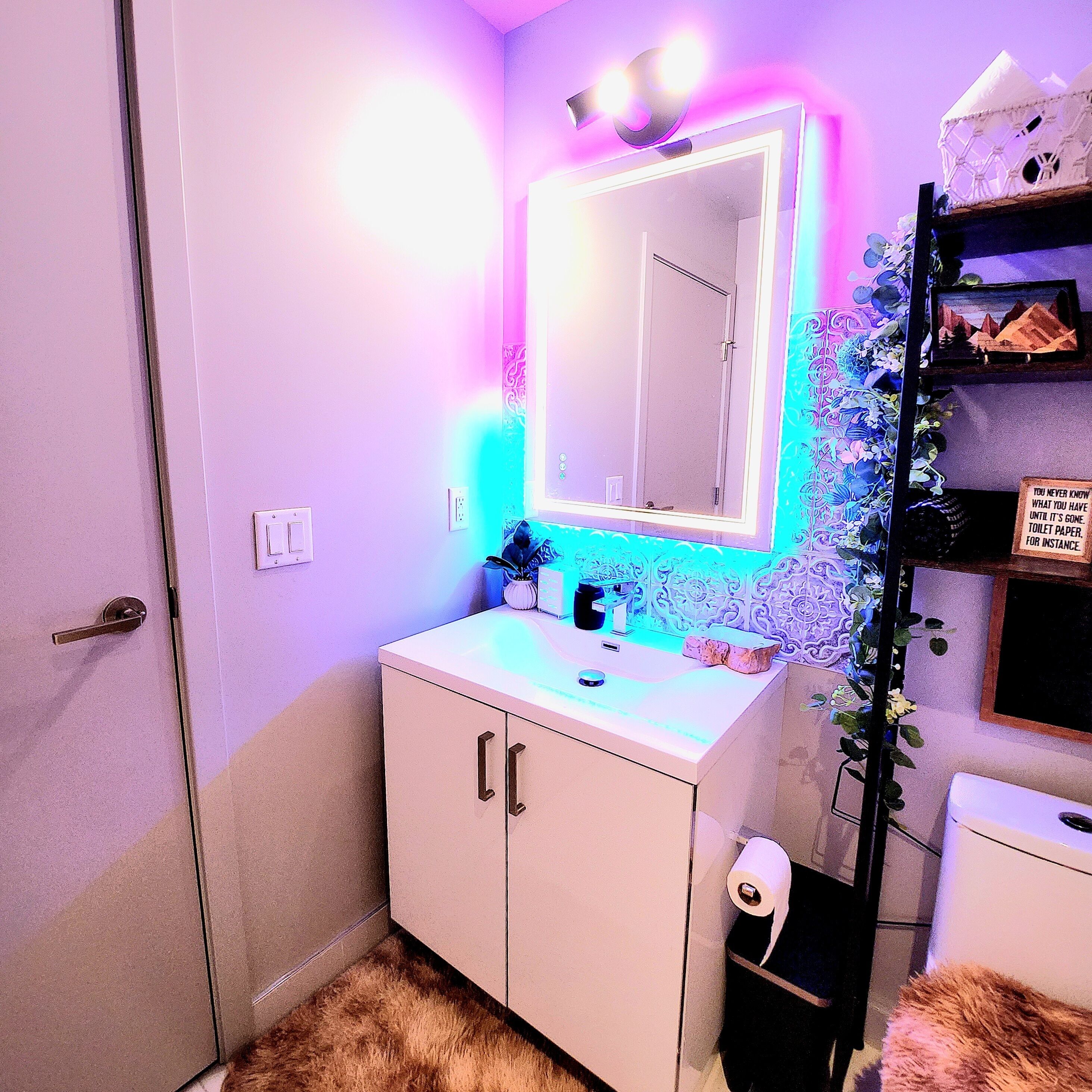 A bathroom with a white sink, a mirror with LED lights, and a toilet paper holder.