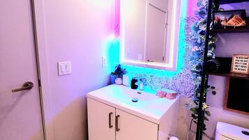 A bathroom with a white sink, a mirror with LED lights, and a toilet paper holder.