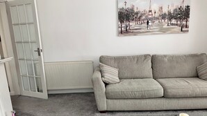 Un saló amb un sofà gris, una taula de centre de vidre, un quadre d'un paisatge urbà i un radiador blanc.