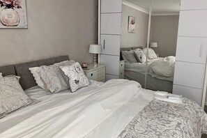 Et soveværelse med seng, natbord, kommode og et spejl.