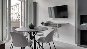 A modern dining area with a round table, four white chairs, a potted plant, a built-in TV, and a minimalist shelving unit. - Farini 74 Design Apartment – Metro M3, WiFi, AC (Milan)
