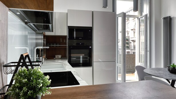 A modern kitchen with built-in appliances, a dining area with a table, and a view of the city through large windows. - Farini 74 Design Apartment – Metro M3, WiFi, AC (Milan)