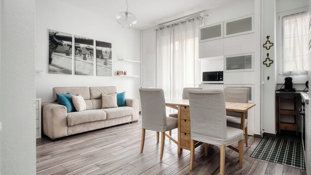 A modern living room with a sofa, dining table, and chairs, a kitchen area with appliances, and a large window with curtains. - Stylish Flat Near San Siro – Metro, WiFi & AC (San Siro)