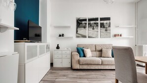 A modern kitchen with white cabinetry, a dining area with a wooden table, and a beige sofa with teal cushions. - Stylish Flat Near San Siro – Metro, WiFi & AC (San Siro)