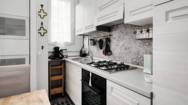 A compact kitchen with white cabinetry, a gas stove, a coffee maker, and a small window. - Stylish Flat Near San Siro – Metro, WiFi & AC (San Siro)