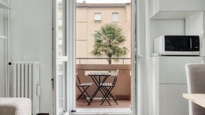 A balcony with a table and chairs, a potted plant, and a white microwave on the right. - Stylish Flat Near San Siro – Metro, WiFi & AC (San Siro)