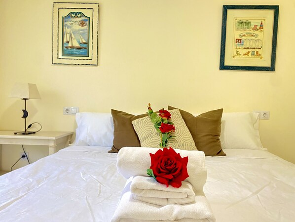 A neatly made bed with white linens, a red rose, and a stack of towels. There are two pillows, one white and one brown. A nightstand with a lamp and a framed picture on the wall above the bed. - TERRACE IN ALTEA ISLAND (altea)