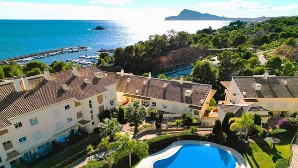 Un resort con una piscina grande, villas frente a la playa y vista al mar.