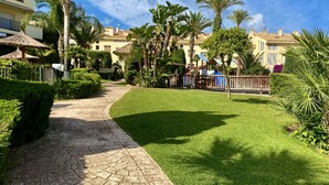 Un sendero pavimentado que lleva a una zona de piscina con palmeras y una valla de madera.