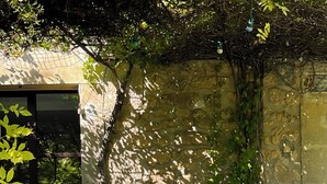 An outdoor seating area with metal chairs and a table, surrounded by a stone wall and greenery.