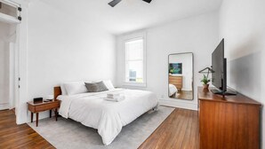 Un dormitorio con cama, mesita de noche, televisor y un espejo grande.