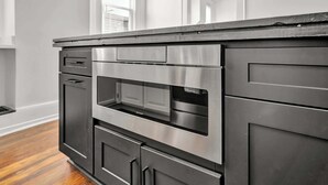 Eine moderne Küche mit eingebauter Mikrowelle und Backofen, Edelstahlgeräten und einer dunklen Arbeitsplatte.