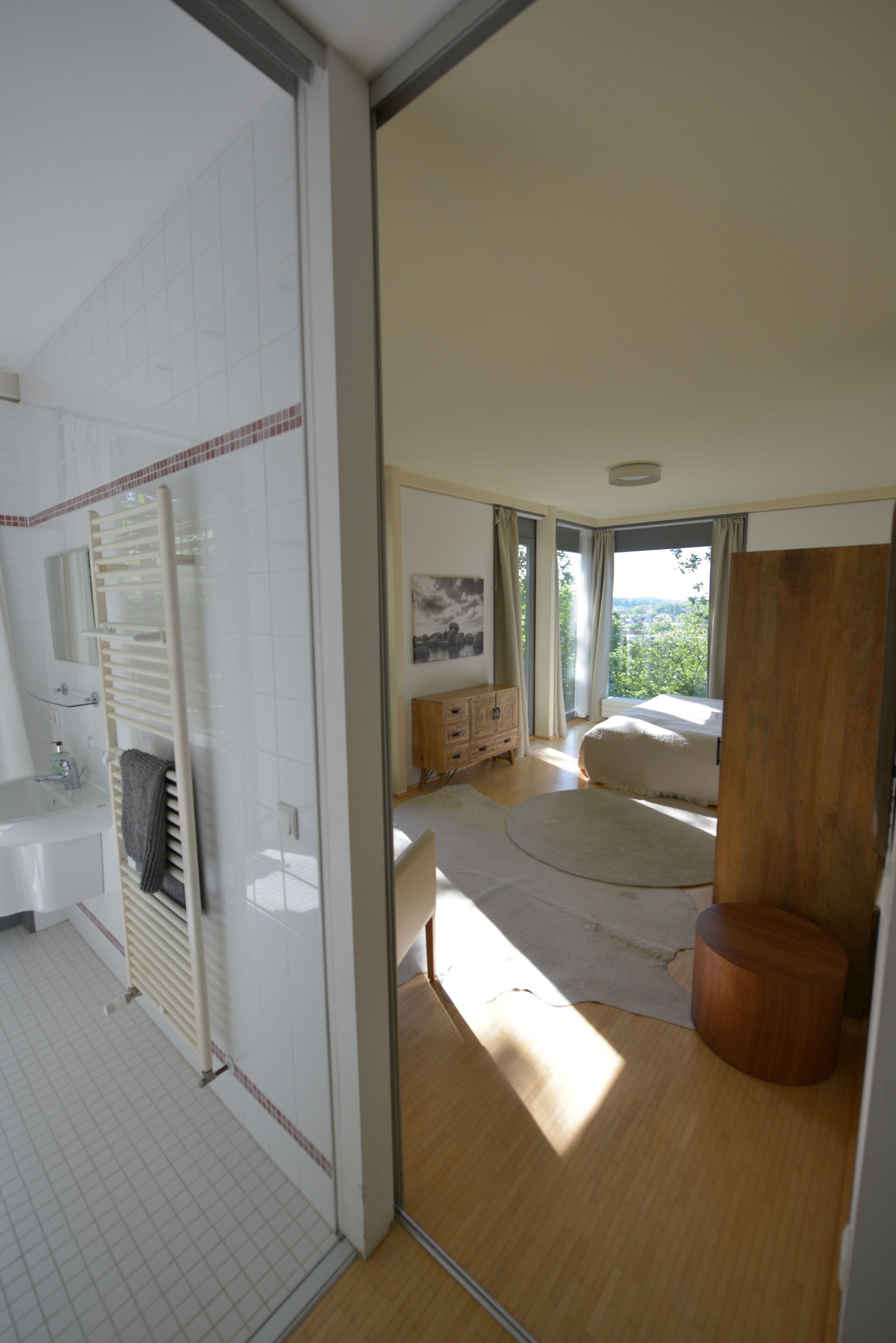 Ein Schlafzimmer mit großem Fenster, Holzboden, Bett, Nachttisch und Spiegel.