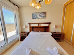 A hotel room with a large bed, two bedside tables, a painting on the wall, and a view through a large window.