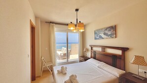 Ein Hotelzimmer mit Bett, Nachttisch, Lampe, einem Gemälde und Meerblick.