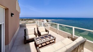 Ein Balkon mit Gartenmöbeln, freier Blick auf das Meer und eine Gebäudefassade.