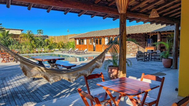 A pool area with a hammock, wooden tables, and chairs. - Pousada Refúgio Verde Trancoso (Porto Seguro)