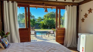 A bedroom with a large bed, wooden ceiling, and a view of a swimming pool and patio furniture. - Pousada Refúgio Verde Trancoso (Porto Seguro)