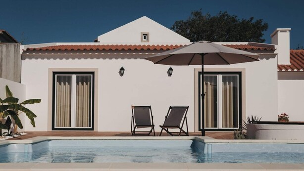 A poolside area with two lounge chairs and an umbrella, a white building with a tiled roof, and a clear blue sky. - Country House (Serra do Bouro)