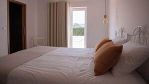 A bedroom with a large bed, a window with curtains, and a hanging light fixture. - Country House (Serra do Bouro)