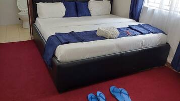 A hotel room with a bed, a red carpet, and a pair of blue slippers on the floor.