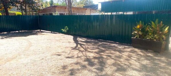 Un espacio al aire libre cercado, con suelo de grava, una planta pequeña y un macetero de madera con flores amarillas.