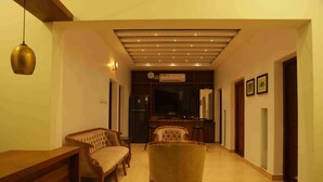 A hallway with a sofa, armchairs, a television, and a ceiling with recessed lighting. - HORTUS MALABARICUS RESORT (Talappilly)
