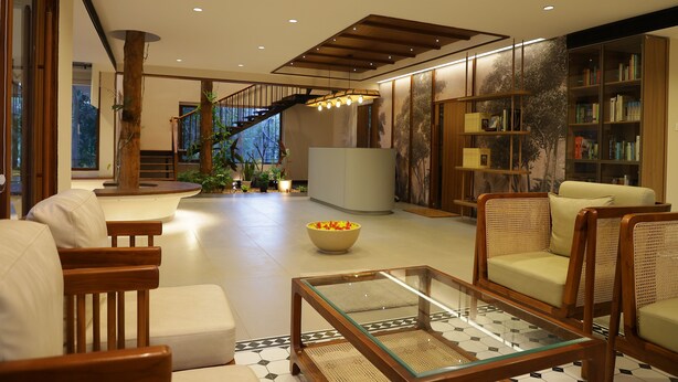 A spacious living area with a staircase, a glass coffee table, and a bookshelf. - HORTUS MALABARICUS RESORT (Talappilly)