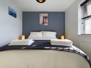Una cama bien tendida con sábanas blancas y dos lámparas de noche.