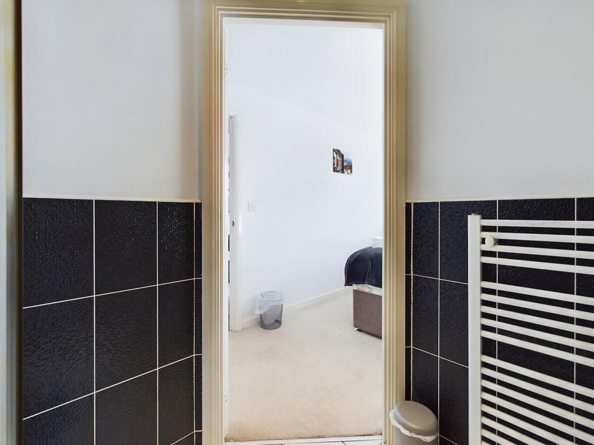 A bathroom with black and white tiles, a white radiator, and a door leading to another room.