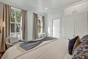 A bedroom with a bed, a chair, a wardrobe, and a window with curtains.