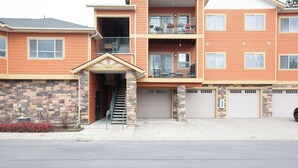 A multi-story residential building with a stone facade, a front entrance with a staircase, and a garage. - Stylish 3-bed, 2-bath modern condo in Coeur d'Alene, perfect for up to 6 guests. Enjoy a fully equipped kitchen, king suite, and community steam sauna & gym. 12 mins from downtown CDA, 20 mins to Silverwood Theme Park, and 40 mins to Spokane! (Coeur d'Alene)