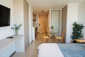 A hotel room with a bed, bedside table, TV, and a small dining area with chairs and a table.