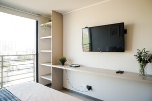 A modern room with a TV mounted on the wall, a balcony with a plant, and a small shelf with a plant and a device.