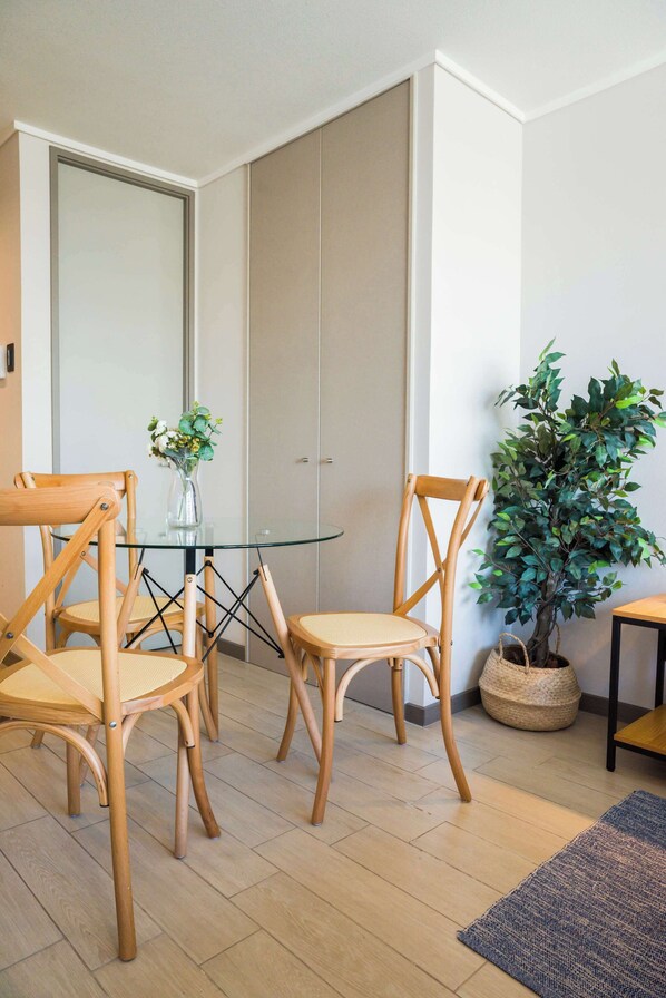 Une pièce comprenant une table à plateau en verre, deux chaises en bois, une plante en pot et un panier tressé.