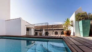 A swimming pool with a wooden deck, a white building with a tiled roof, and potted plants. - Casa de Medina: a spacious Andalusian townhouse in the heart of Medina Sidonia (Medina-Sidonia)