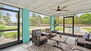 A sunroom with wicker furniture, a ceiling fan, and large windows offering a view of a backyard with bicycles. - Tropical Oasis for your Naples Getaway!  (Naples)