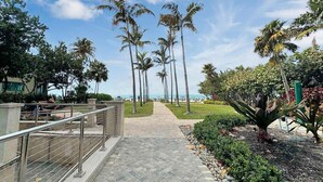 A pathway lined with palm trees leading to a beach, with a railing on one side and a landscaped area with plants on the other. - Tropical Oasis for your Naples Getaway!  (Naples)