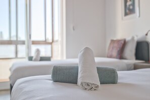 Ett hotellrum med två sängar, utsikt över staden och en väl bäddad säng med en hoprullad handduk.