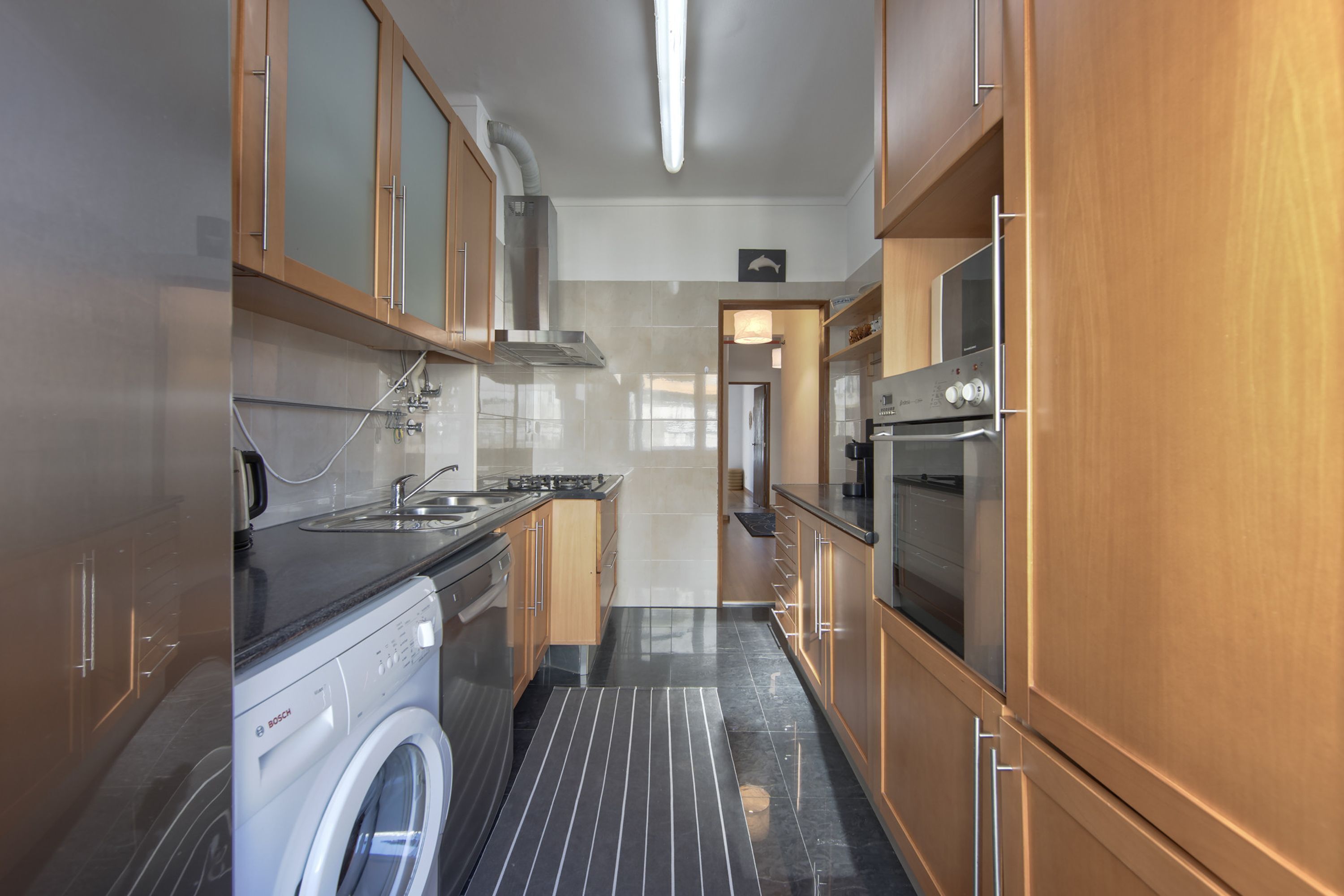 A modern kitchen with wooden cabinets, a Bosch washing machine, a stainless steel sink, and a built-in oven.