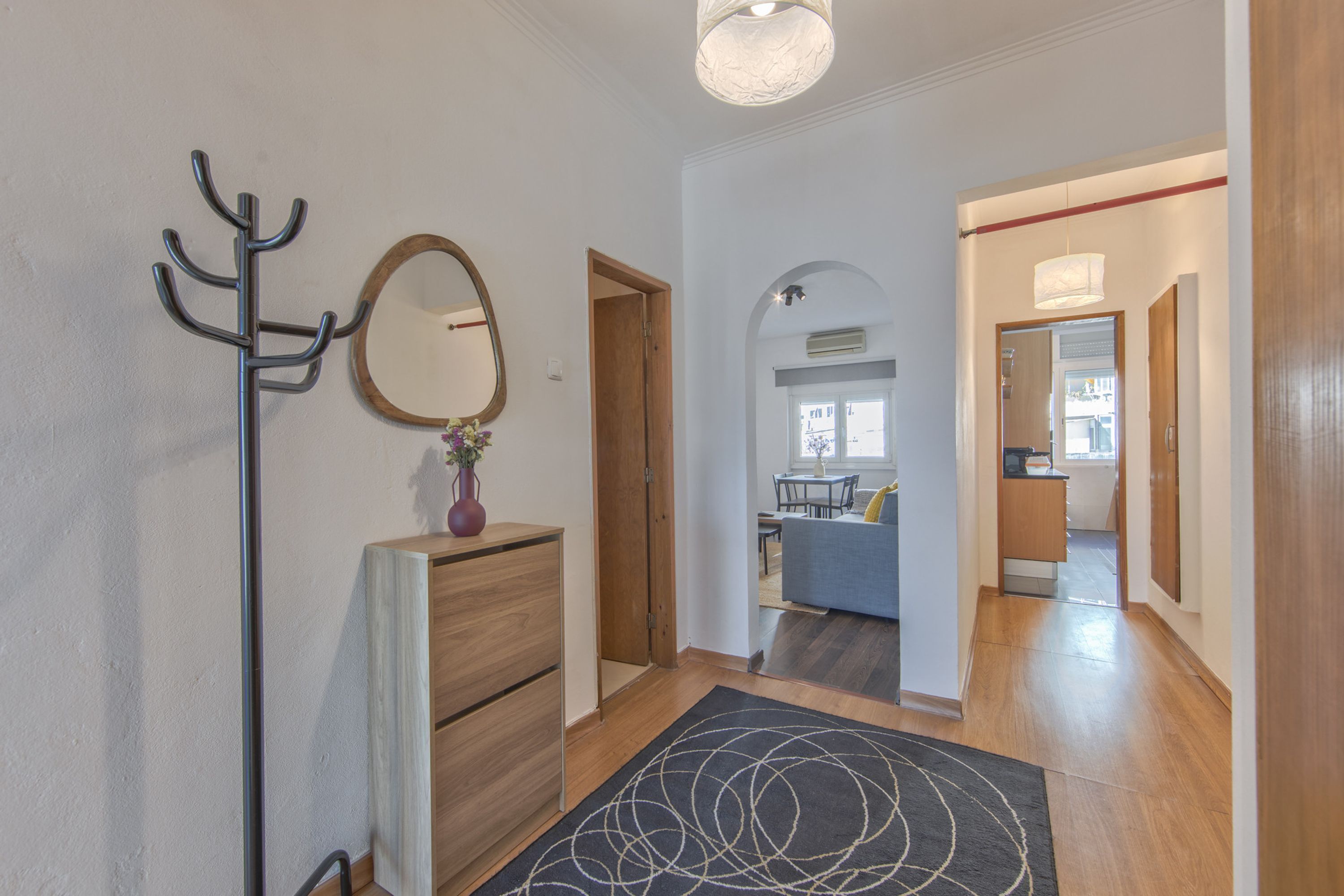 A hallway with a coat rack, a mirror, a wooden dresser, and a rug.