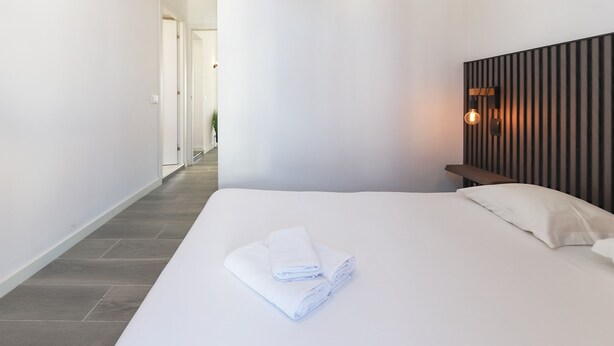 A hotel room with a neatly made bed, a wooden headboard, and a wall-mounted light fixture. - Rato Prime Terrace BY Homing (Lisbon)