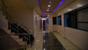 Passadís d'hotel modern amb sòl de marbre, escala amb barana metàl·lica i sostre amb il·luminació encastrada i tires LED blaves.
