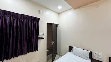 Een hotelkamer met een bed, een nachtkastje, een stopcontact en een deur die naar een andere kamer leidt.