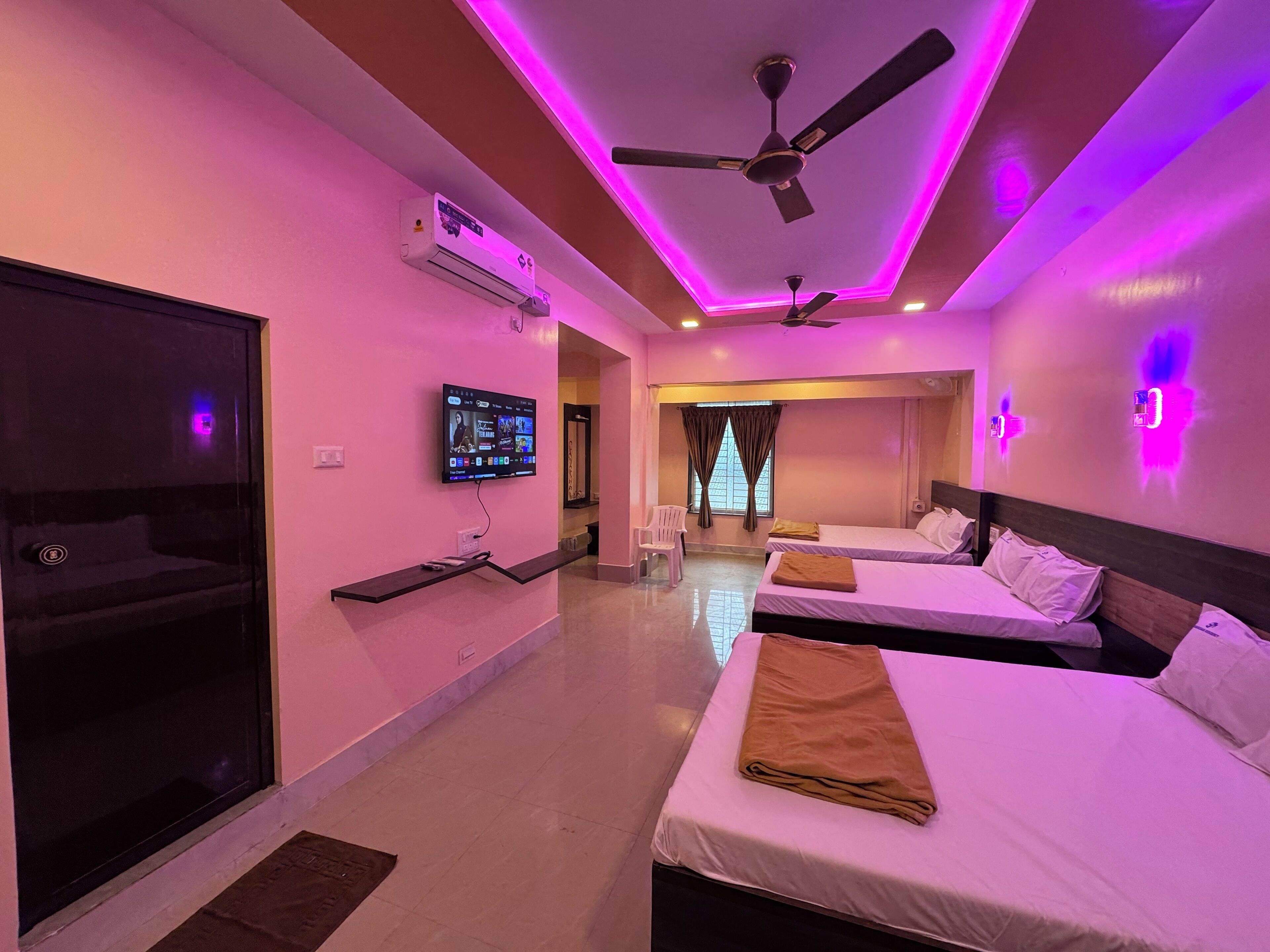 A hotel room with two beds, a TV, ceiling fans, and purple ambient lighting.