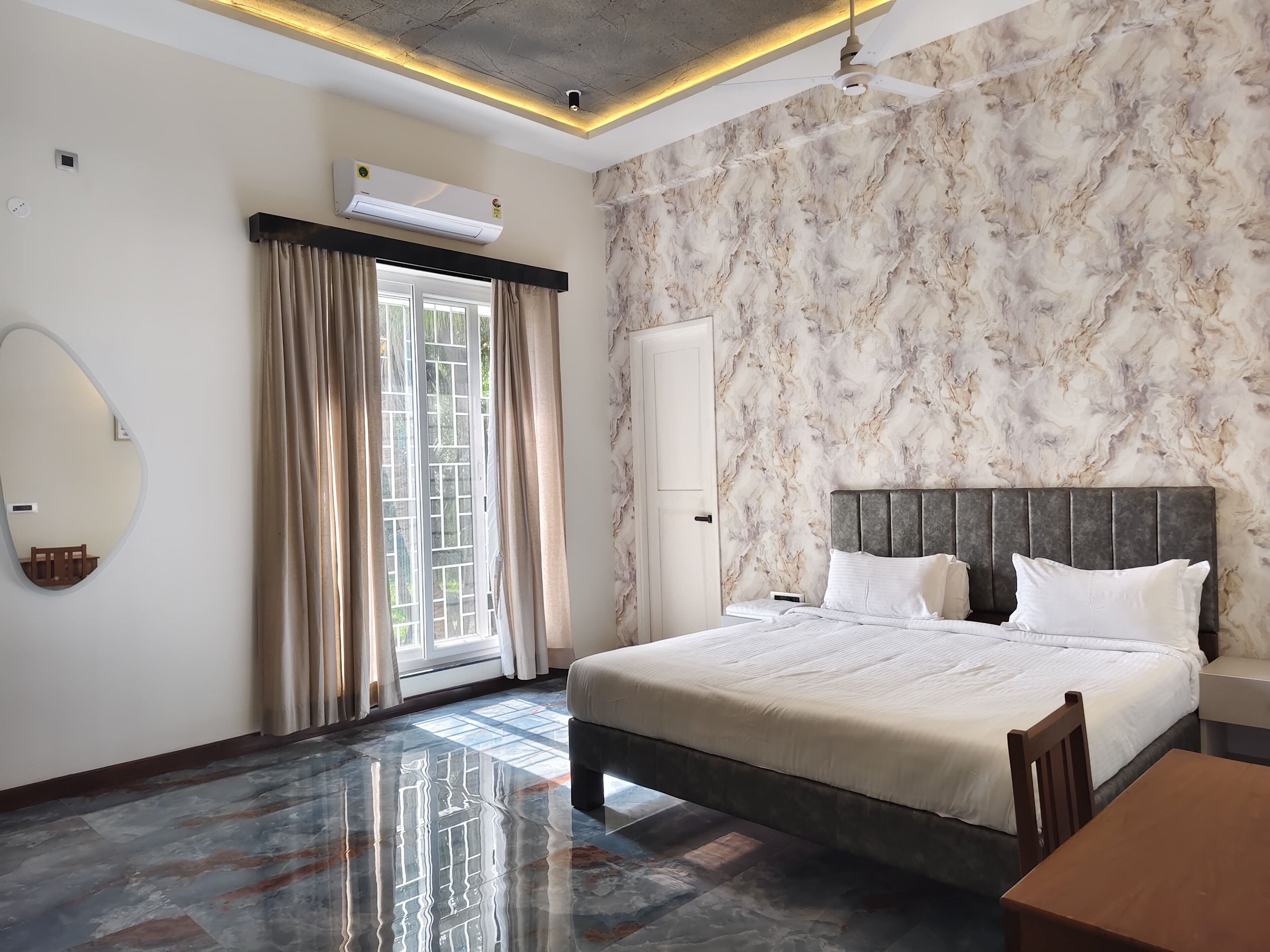A modern hotel room with a marble-patterned wall, a large bed with white bedding, a wooden nightstand, and a ceiling fan.