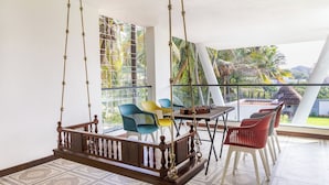 A room with a wooden swing chair, colorful plastic chairs, a table with a foosball table, and a view of the outdoors. - The Serene Shores - Luxury Private Villa (Vanur)