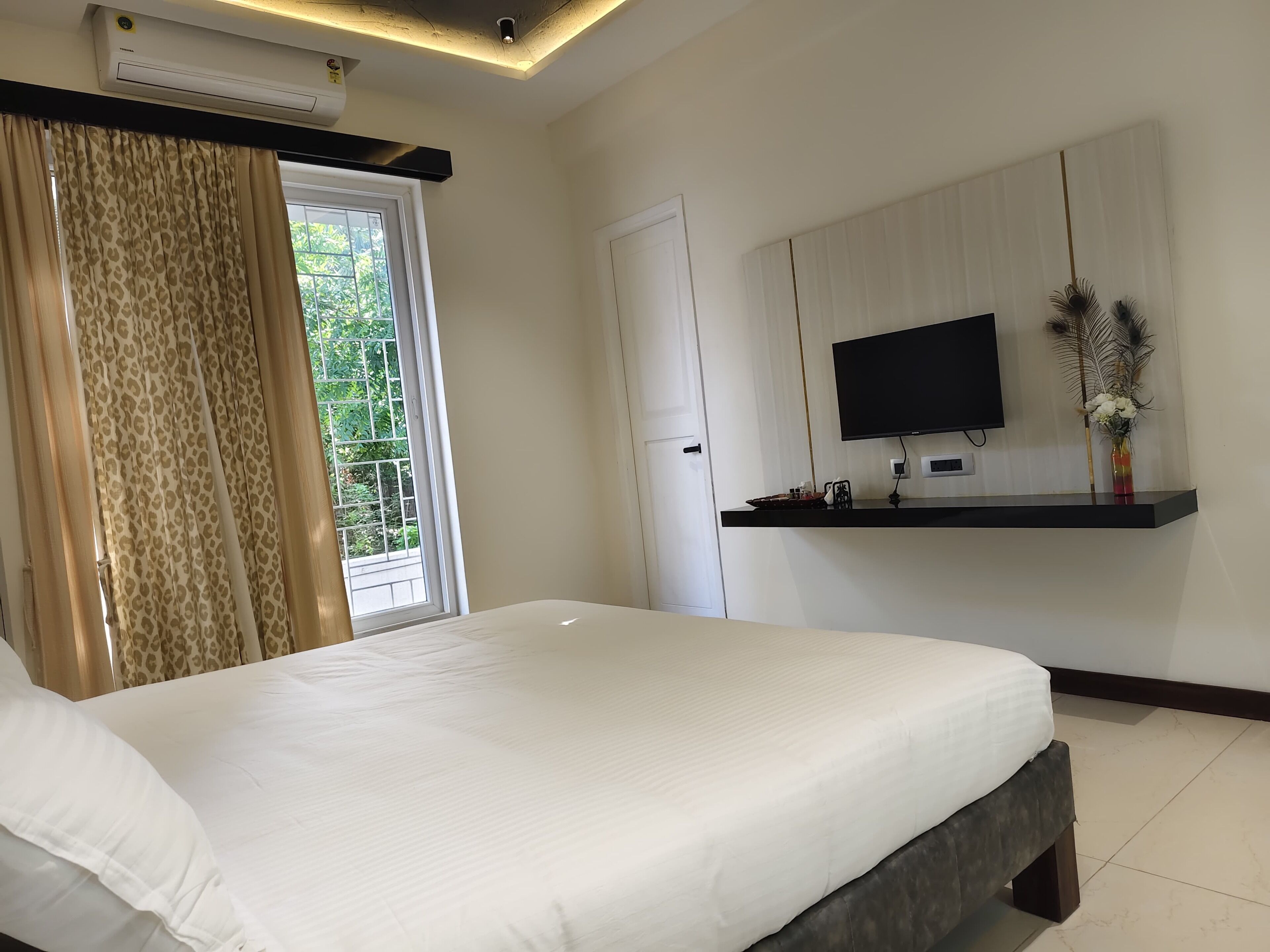 A bedroom with a bed, a TV mounted on the wall, and a window with curtains.