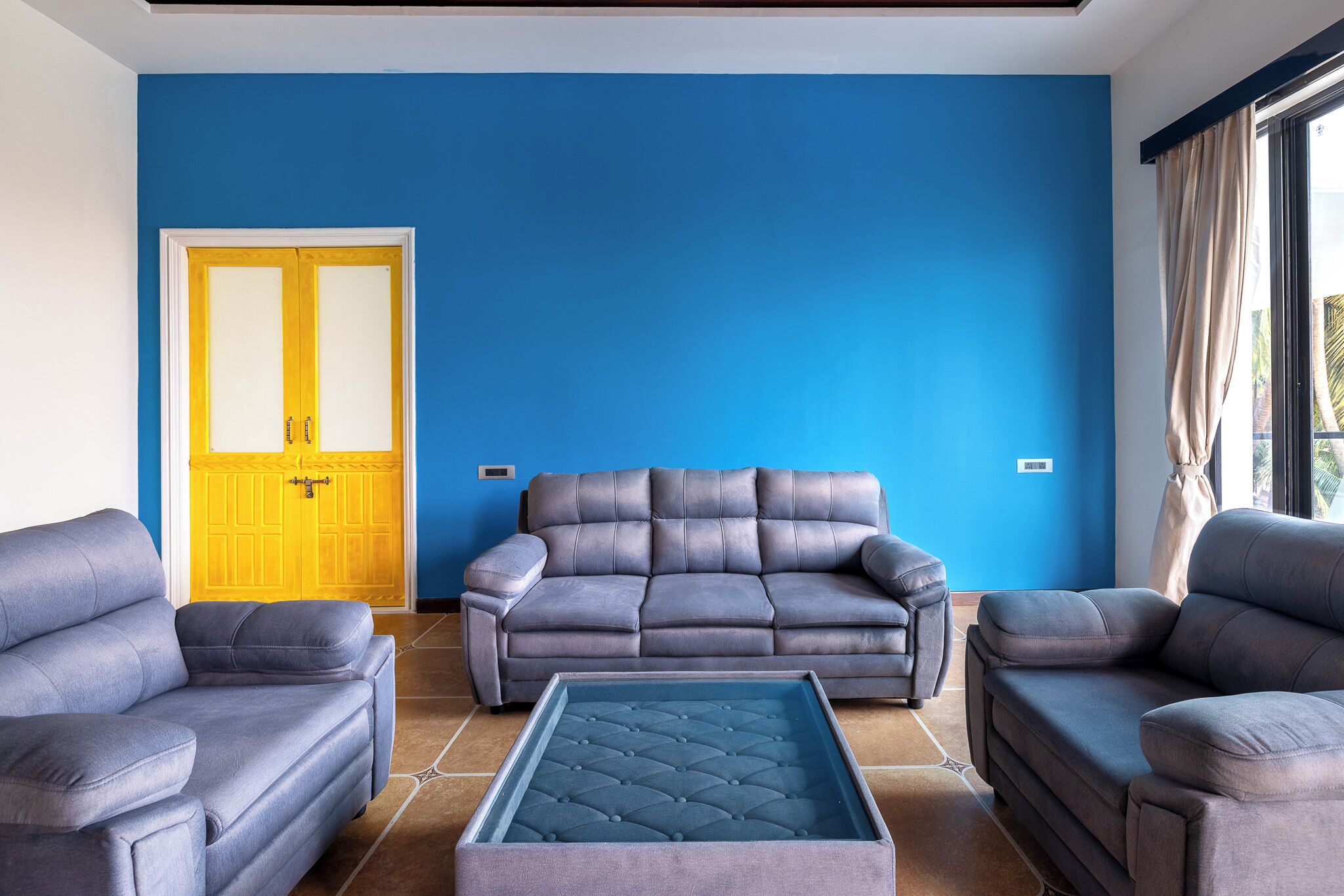 A living room with a blue wall, a grey sofa, and a matching ottoman.