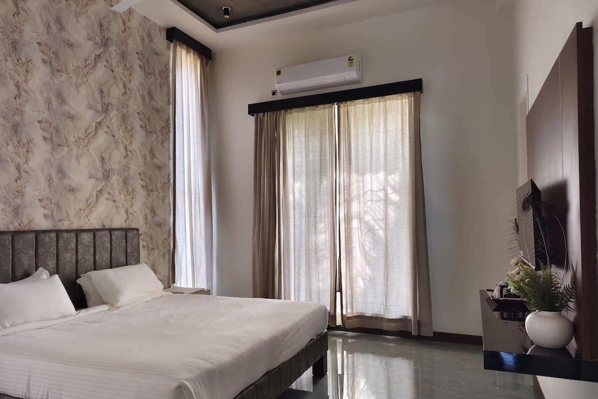 Ein modernes Hotelzimmer mit Wand im Marmor-Design, einem großen Bett mit weißen Leinen, einem Deckenventilator, einer Klimaanlage und einem großen Fenster mit transparenten Vorhängen.